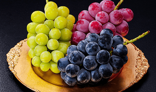 Which fruit grows in heavy clusters on woody vines and is widely cultivated to produce fine wines and raisins?
