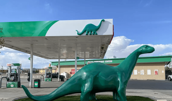 Which famous gas station brand featured a friendly green dinosaur on its classic roadside sign?